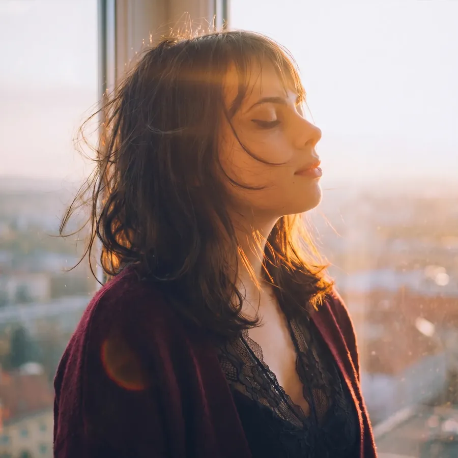 Lily by a window at sunset with the city behind her